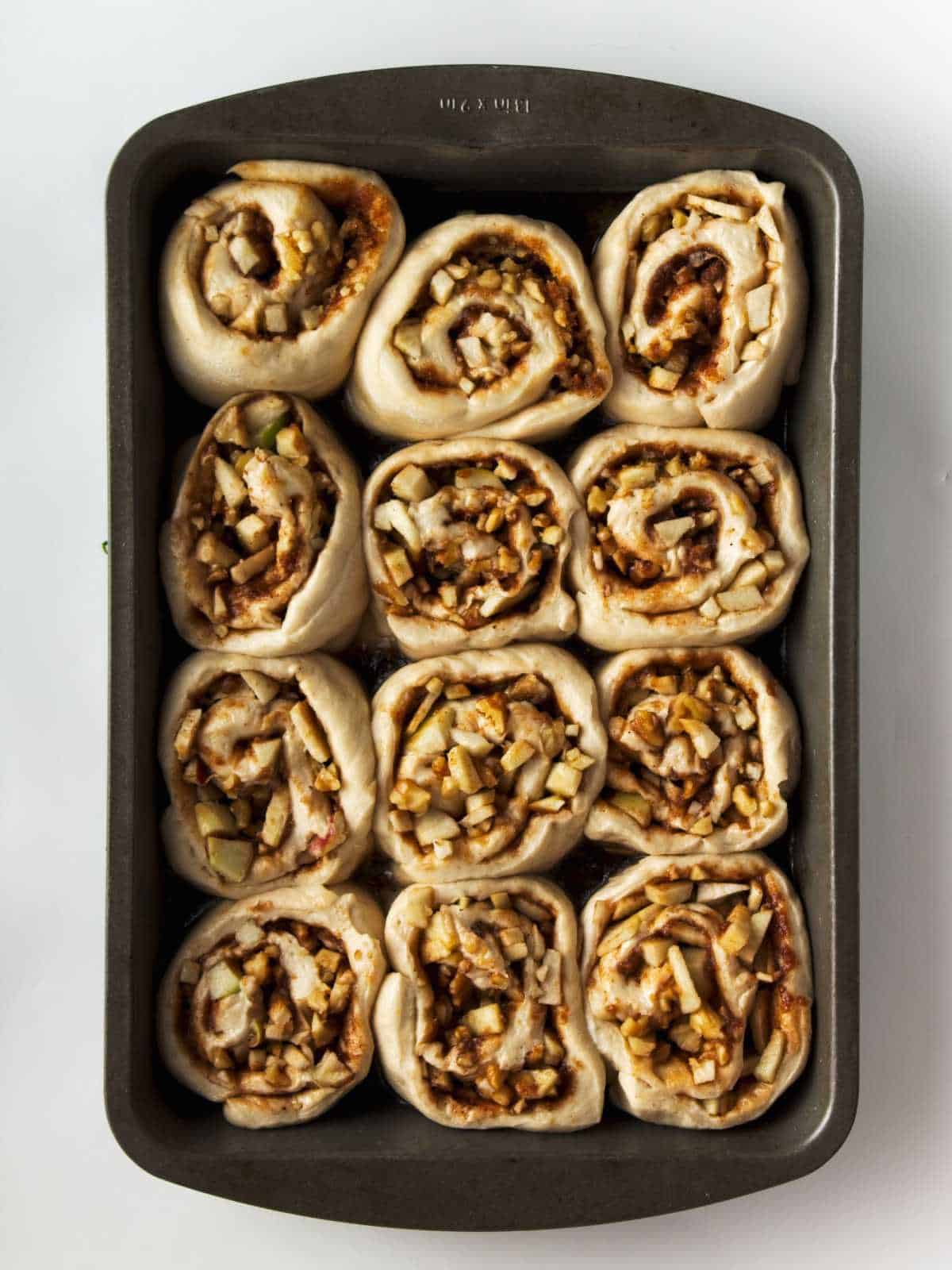 sliced dough pinwheels placed in a baking pan to rise before baking.