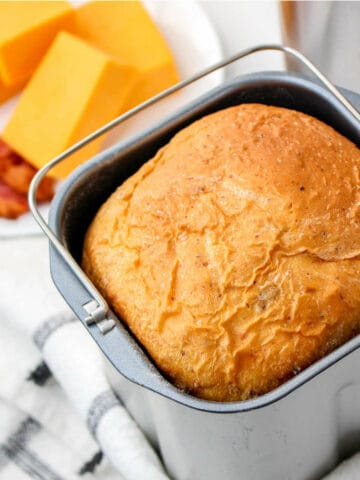 bread maker pan with a baked loaf of cheddar cheese bread.