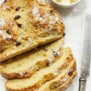 Soda bread with raisins sliced on a table with cubes of butter.