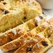 Soda bread with raisins sliced on a table with cubes of butter.