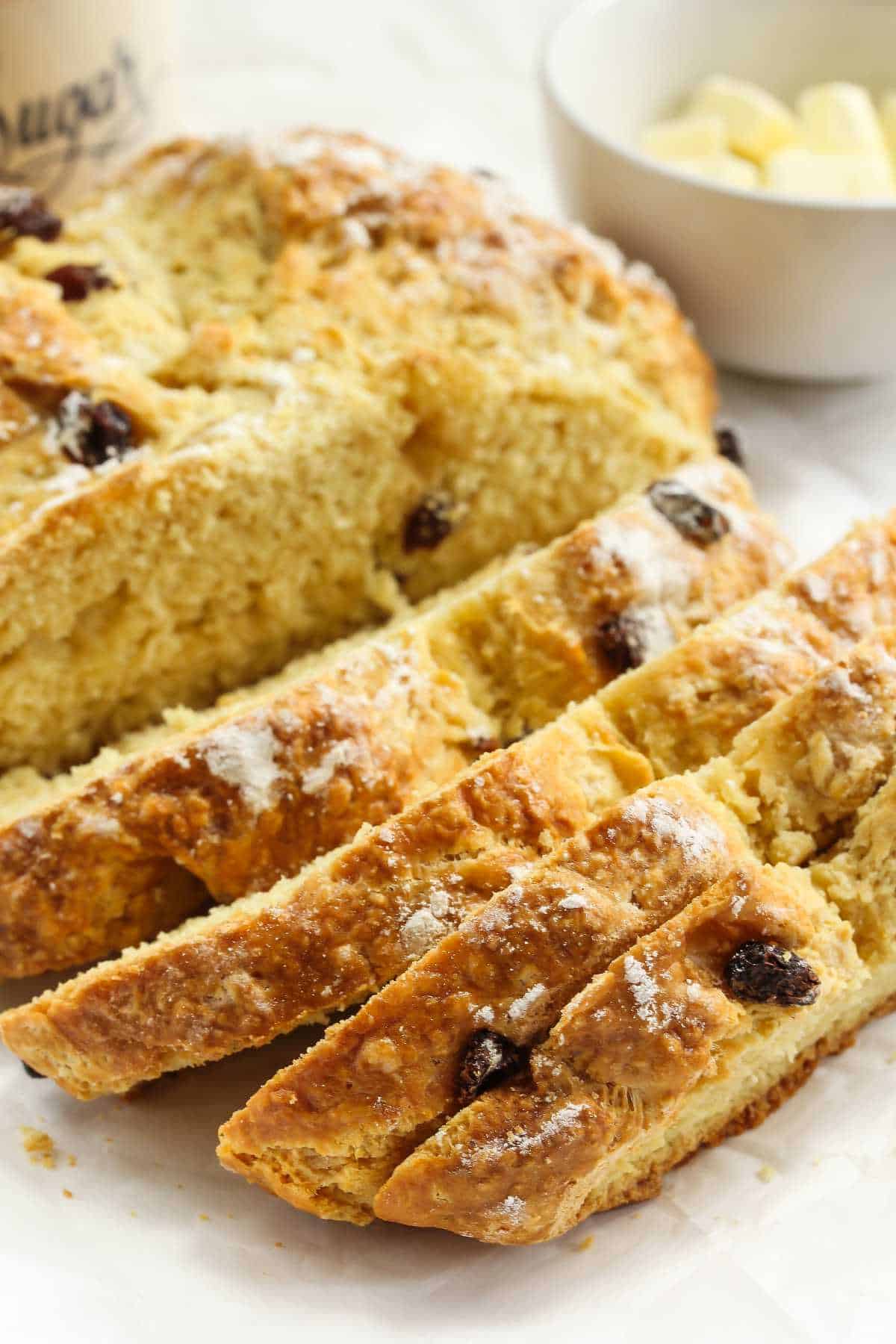 Soda bread with raisins sliced on a table with cubes of butter.