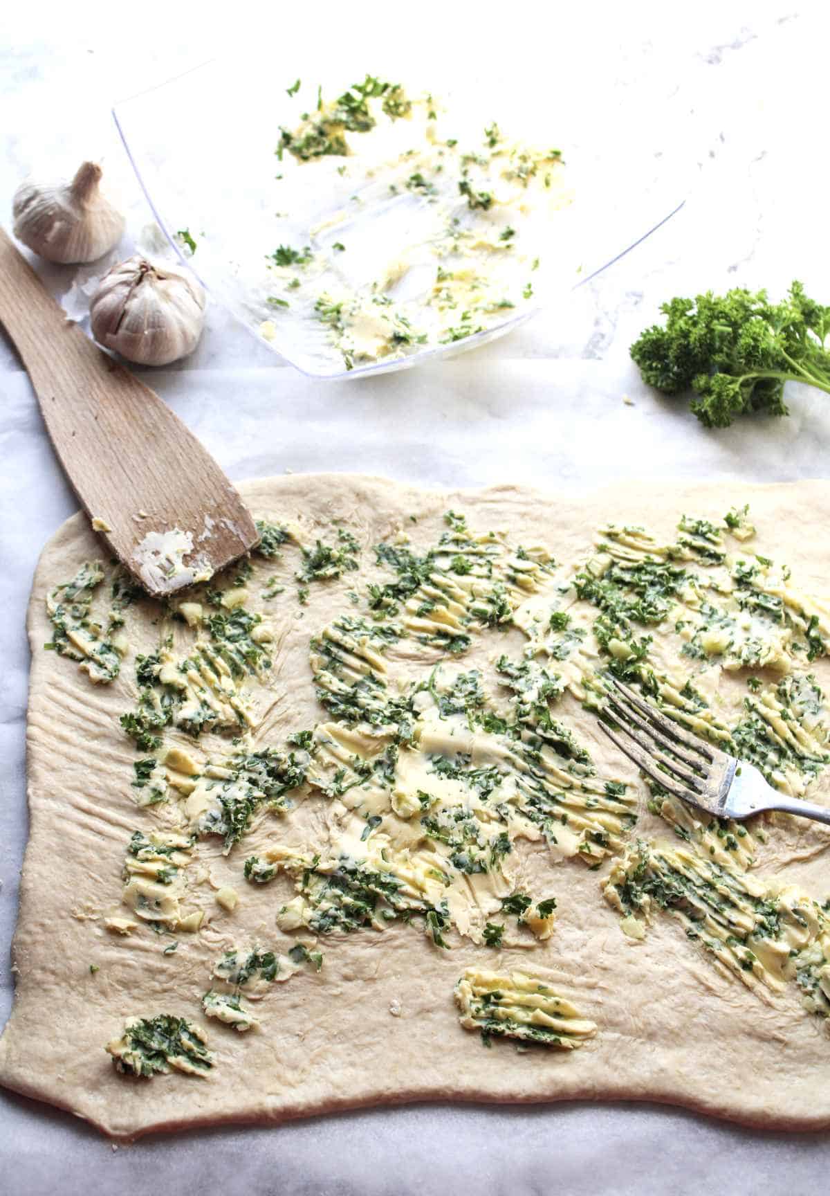 Spreading garlic butter and herbs on a sheet of rolled out bread dough.