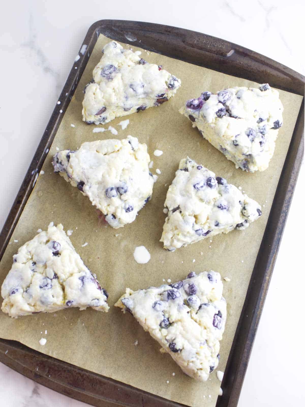 cream brushed scone wedges on a baking sheet.