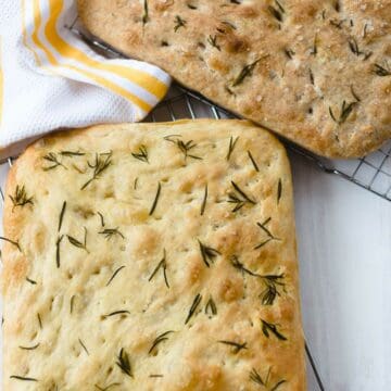 rosemary focaccia on a white surface and yellow kitchen towel.