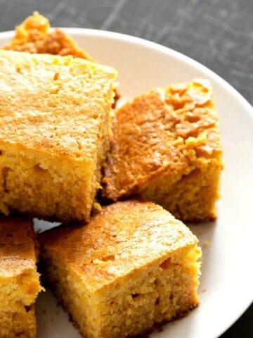 Honey butter cornbread slices stacked on a plate.