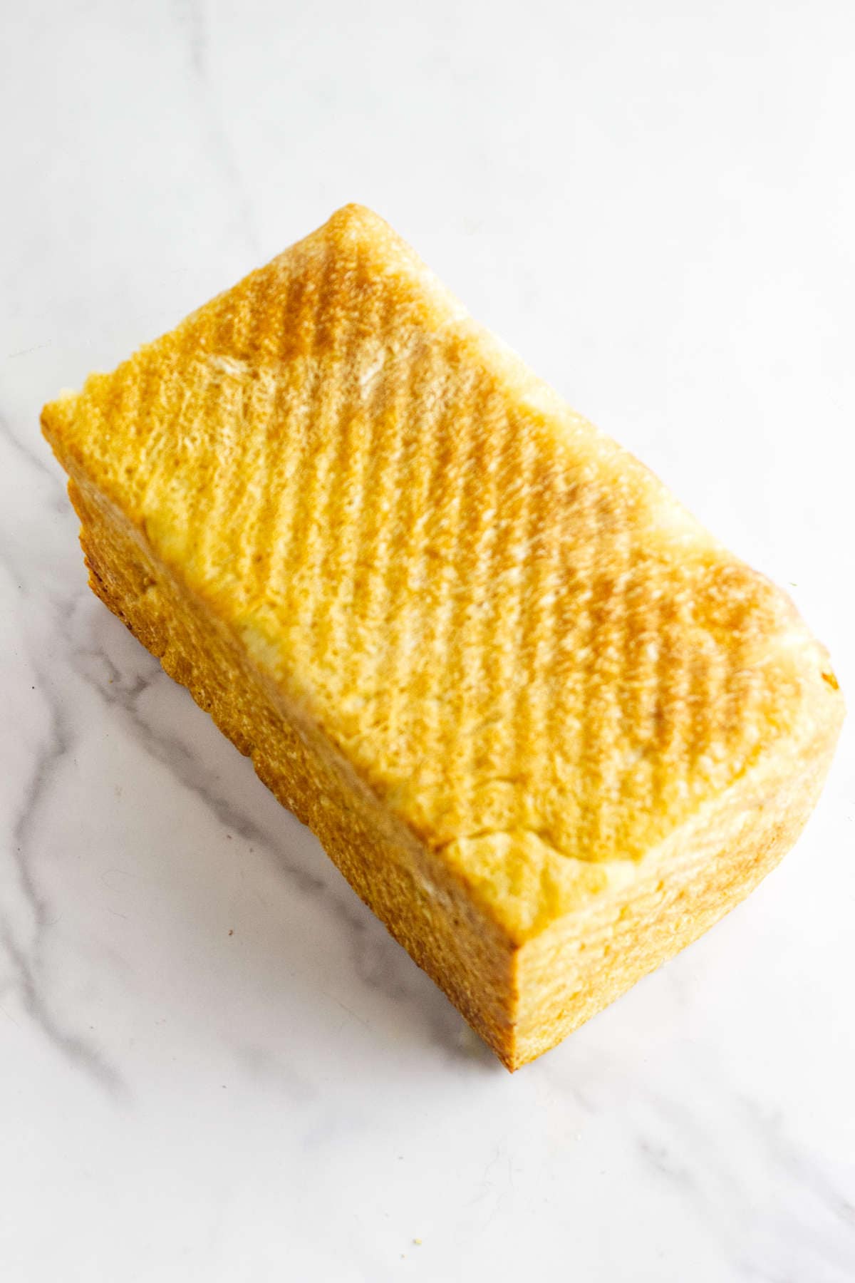A loaf of golden-yellow Pullman bread loaf with a textured top, resting on a light marble surface.