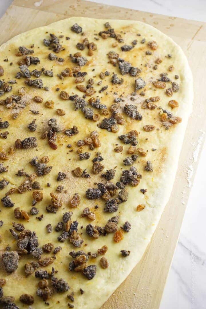 A sheet of dough is rolled out on a wooden surface, topped with raisins, sugar, and cinnamon, reminiscent of the festive flavors found in a traditional rosca de reyes.
