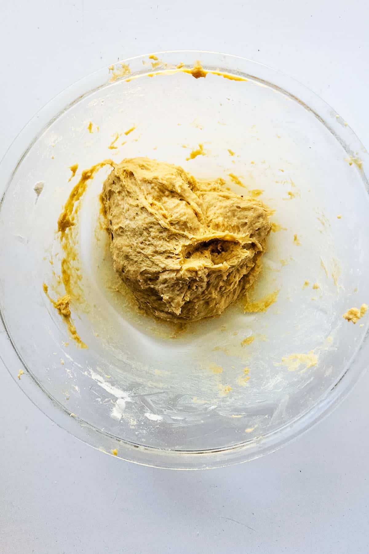A clear glass bowl containing yellowish brioche boule dough on a white surface. The sticky dough clings unevenly to the sides of the bowl, hinting at its potential to become a delightful chocolate brioche loaf.