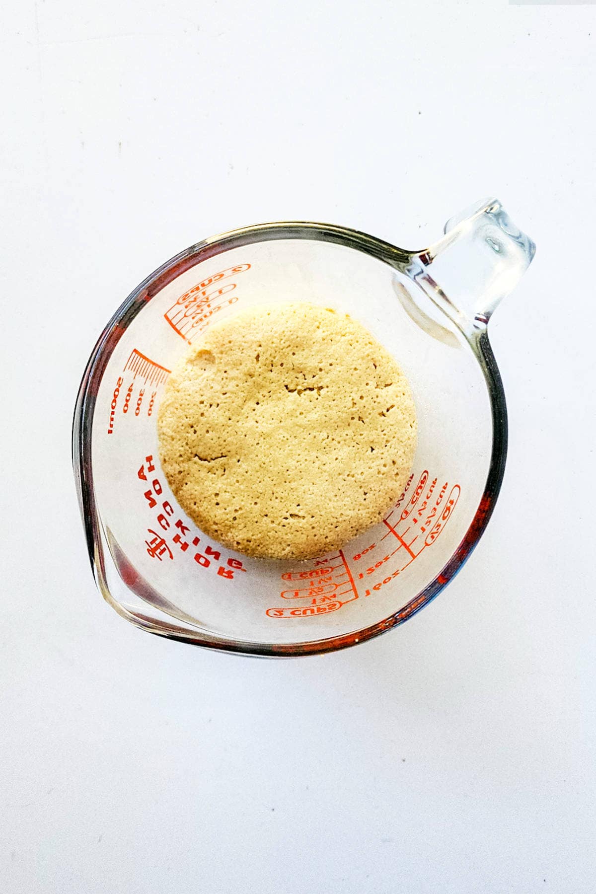 A brioche boule sits cozily in a glass measuring cup with red measurement markings, set against a crisp white background.