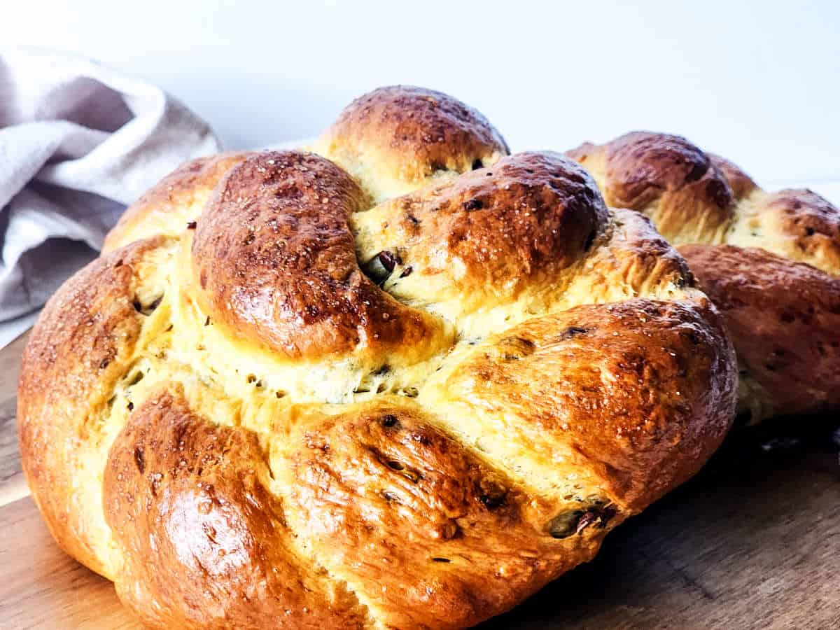 A close-up of a freshly baked, golden-brown brioche boule with a shiny crust rests on a wooden surface. A light-colored cloth is partially visible in the background, enhancing the warm and inviting feel.