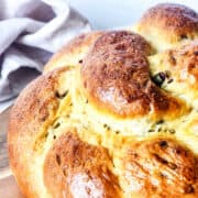 Close-up of a freshly baked, golden-brown chocolate brioche with a textured crust. A beige cloth is partially visible in the background, adding warmth to the scene.