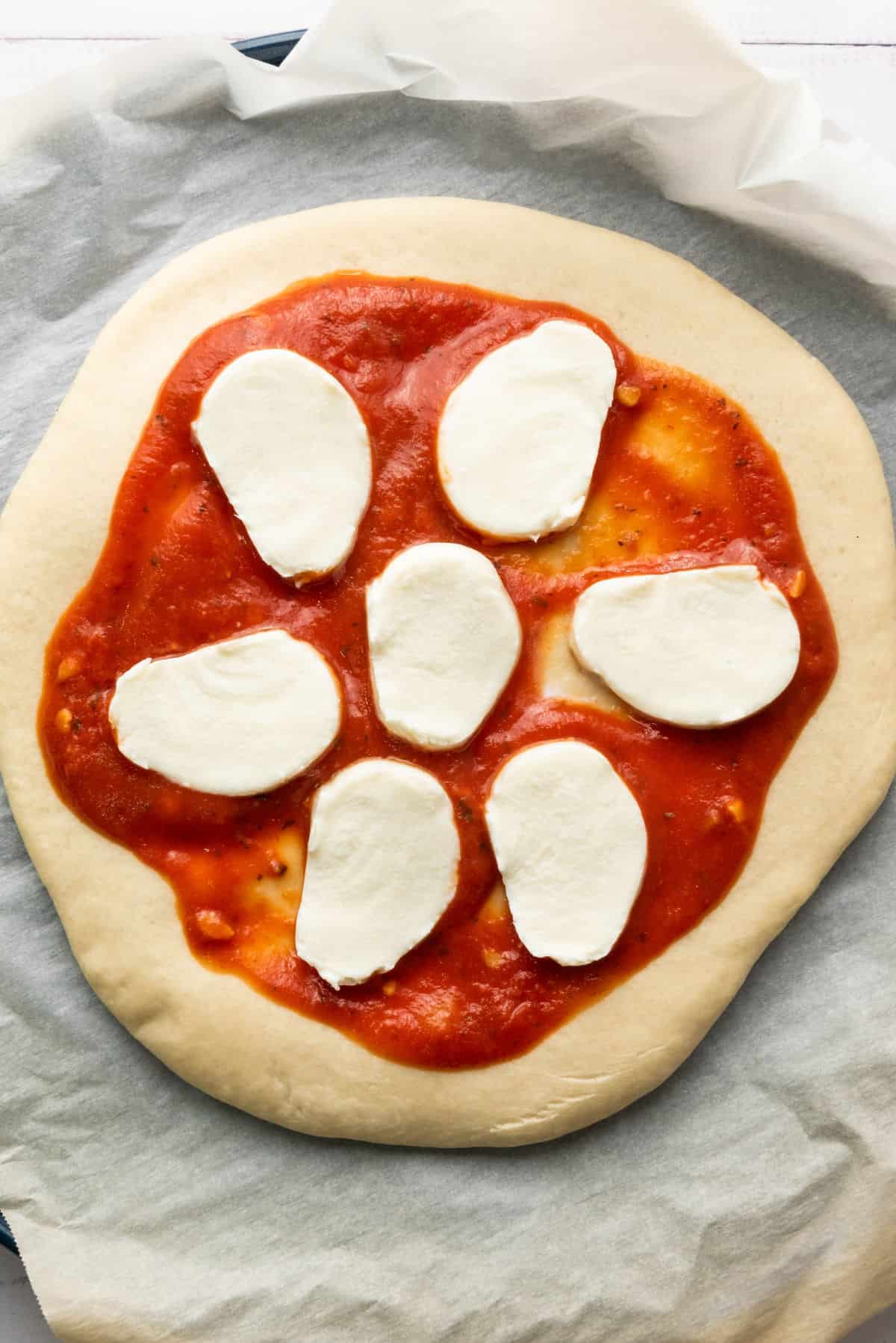 Unbaked thick crust pizza with tomato sauce and seven slices of mozzarella cheese on a round dough placed on parchment paper.
