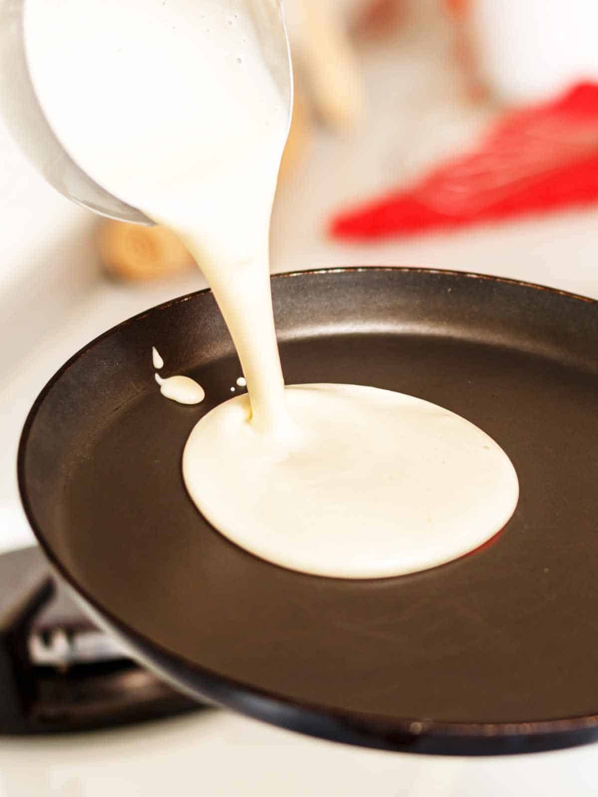 A close-up of old fashioned buttermilk pancake batter being poured from a bowl onto a hot, nonstick frying pan, ready to cook.