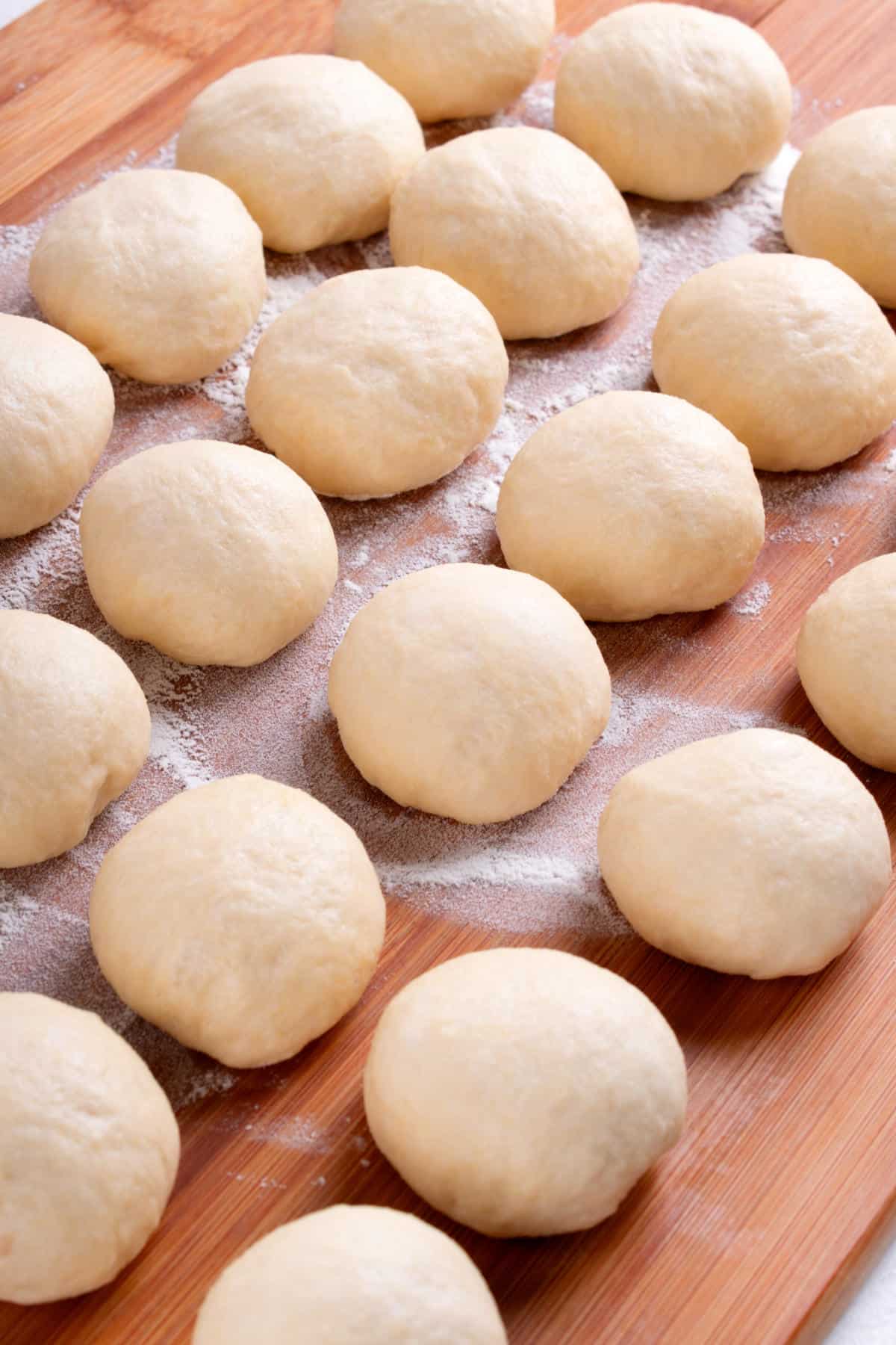 Round balls of dough, destined to become potato flake sourdough rolls, are arranged in rows on a floured wooden surface, ready for baking or cooking.