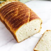 A loaf of sliced potato flake sourdough bread with a golden-brown crust sits on a white surface, with one slice lying next to it.