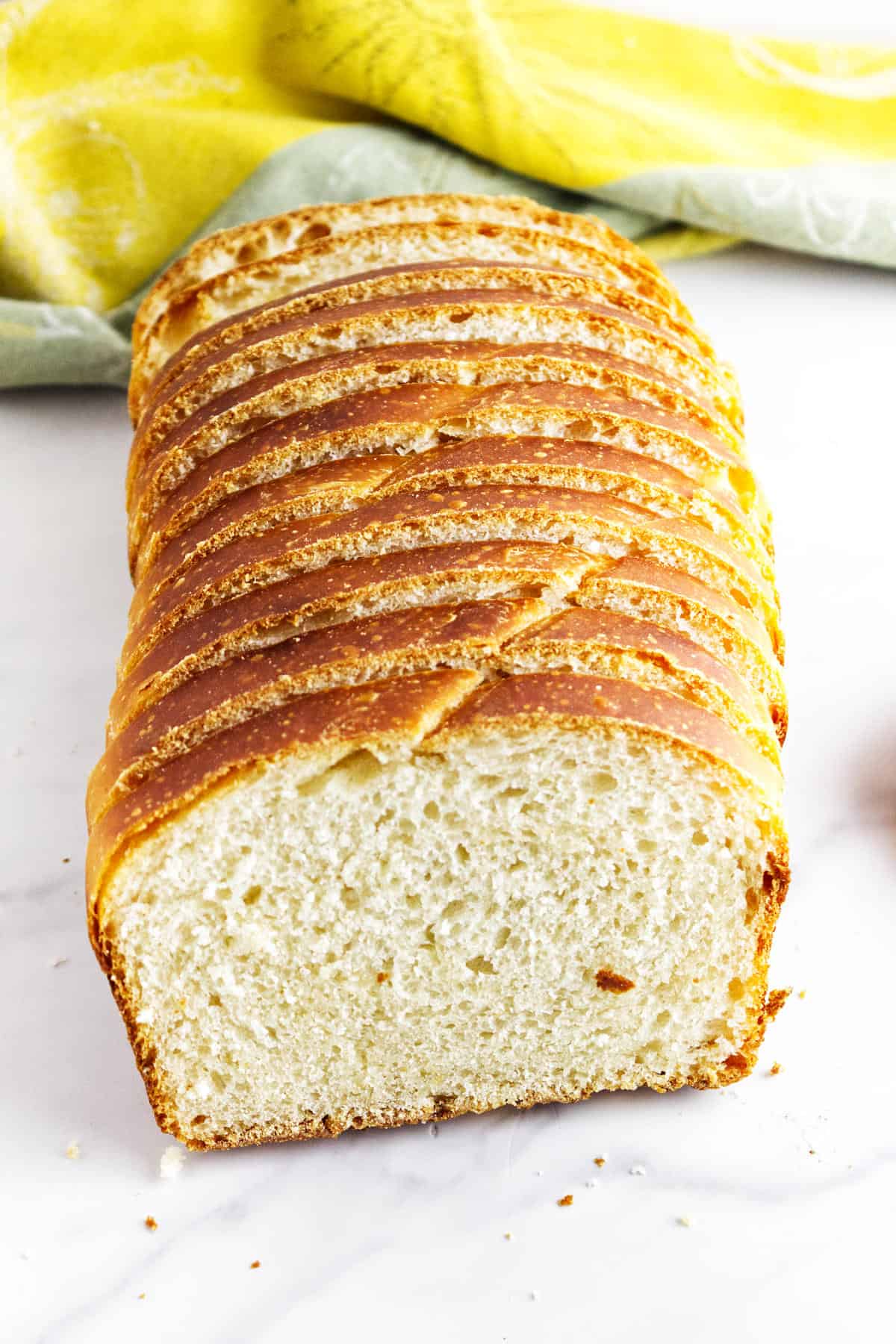 A loaf of homemade potato flake sourdough bread, sliced and arranged on a marble surface, with a yellow and green cloth in the background.