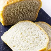 A loaf of homemade white sourdough discard sandwich bread sits on a black cutting board, with two slices cut and laid in front, revealing the soft, airy texture inside.