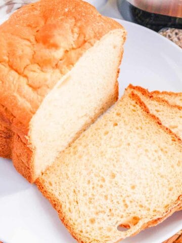 A loaf of homemade bread machine buttermilk bread with two slices cut, arranged on a white plate. The bread looks soft inside with a golden-brown crust.
