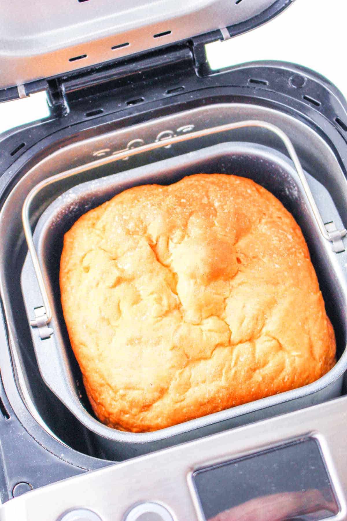 A freshly baked loaf of bread machine buttermilk bread sits inside an open bread machine, displaying a golden-brown crust and soft texture.
