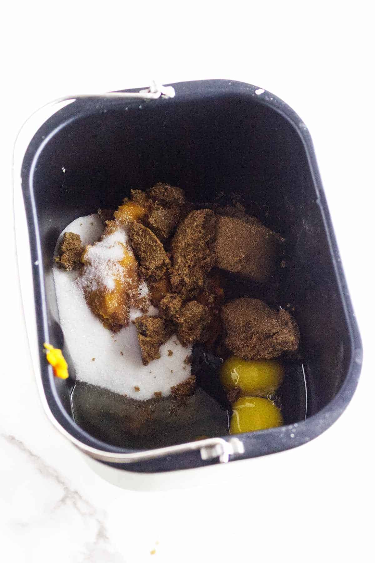 A bread machine pan containing brown sugar, white sugar, eggs, and other baking ingredients is ready to be mixed for delicious bread machine pumpkin bread.