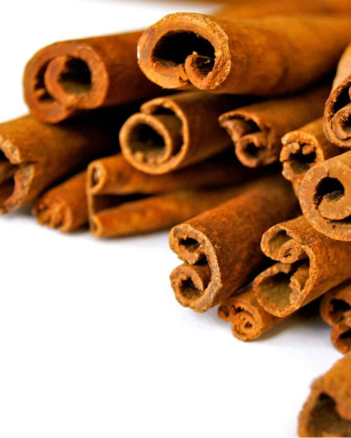 A close-up view of several Cinnamomum cassia, or Saigon cinnamon quills. stacked together on a white surface.