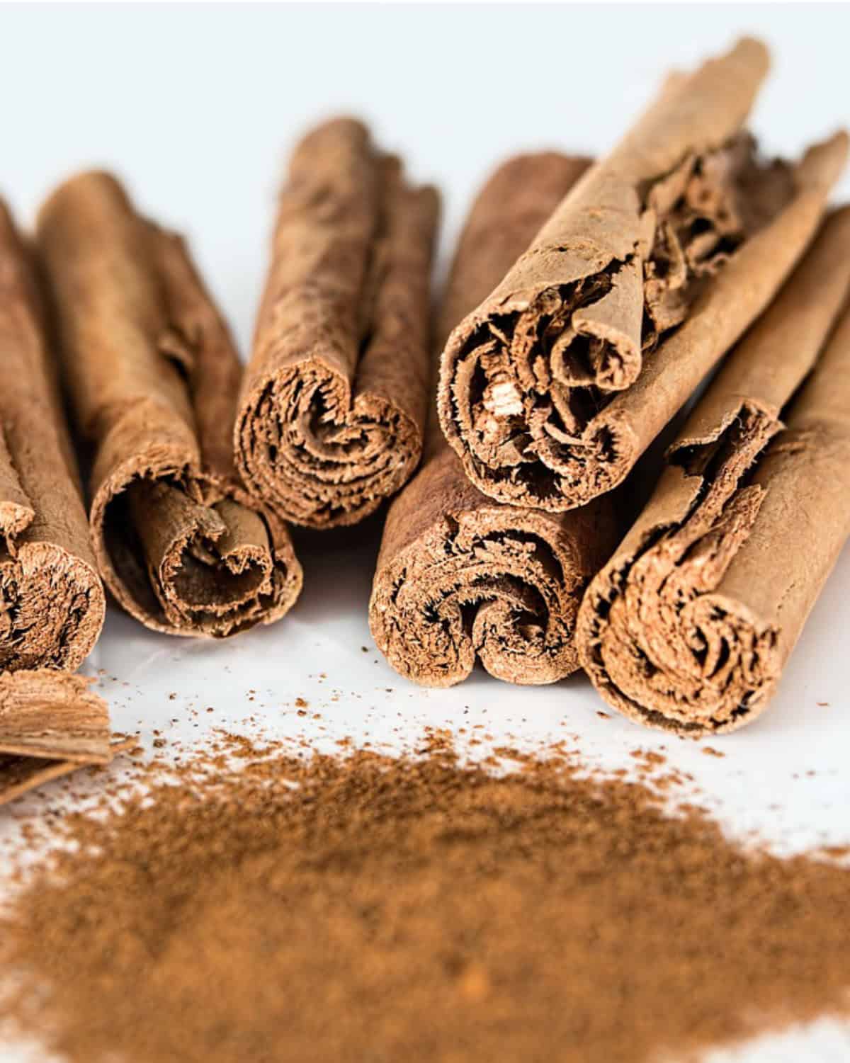 Several Cinnamomum verum - true cinnamon quills sticks are arranged closely together on a white surface.