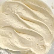 Close-up of smooth, creamy white cream cheese frosting with soft swirls and peaks, showing a light and airy texture.