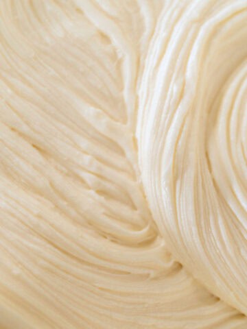 Close-up of smooth, creamy, light-colored cream cheese frosting with visible swirled and textured patterns.
