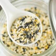 A white spoon holds everything bagel seasoning blend—sesame seeds, poppy seeds, dried garlic, dried onion, and salt—over an open glass jar filled with the same flavorful mixture.