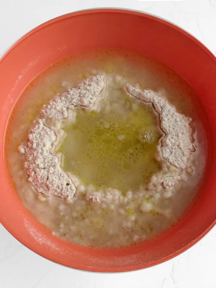 A red mixing bowl containing flour, melted butter, and liquid ingredients—ideal for making whole wheat flour tortillas—partially mixed and not yet fully combined.