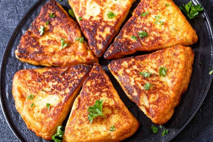 Golden brown, triangular Irish potato pancakes-traditional Irish farls-are arranged in a circle on a dark plate, garnished with fresh parsley.