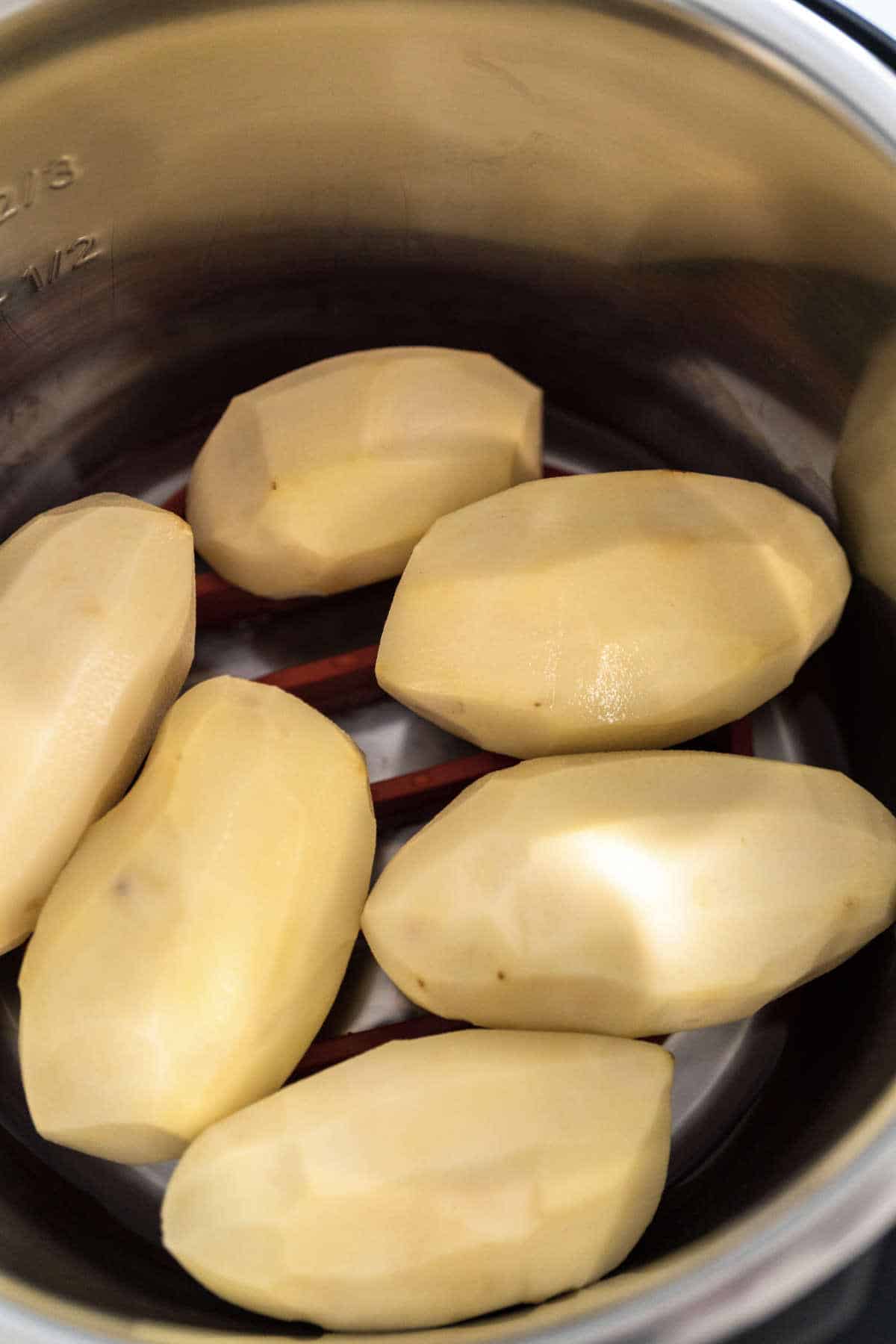 Six peeled potatoes are placed in a stainless steel pot, ready for cooking classic dishes like traditional Irish farls or Irish potato pancakes.