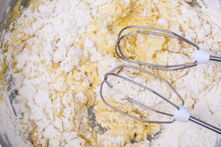 A close-up of electric mixer beaters in a bowl with flour, eggs, and other baking ingredients being mixed into dough or batter for traditional Irish farls or Irish potato pancakes.