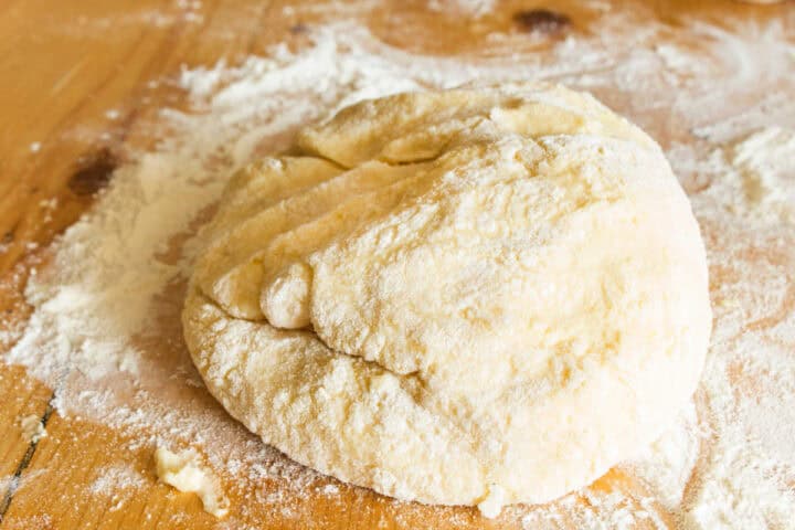 A ball of raw dough sits on a wooden surface dusted with flour, ready to be kneaded or rolled out for authentic Traditional Irish farls.