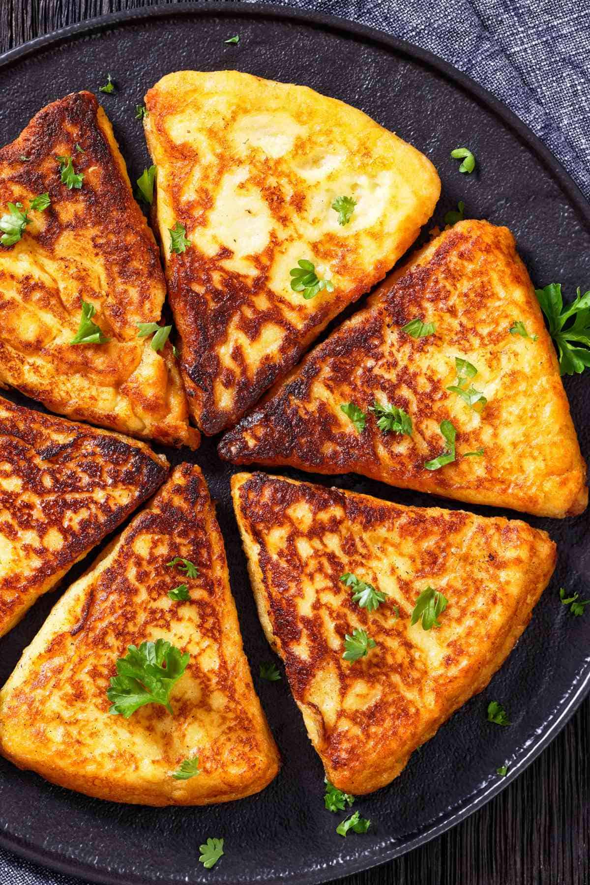 Golden, triangular Irish potato pancakes arranged in a circle on a dark plate, garnished with fresh parsley, with a rustic blue cloth in the background.