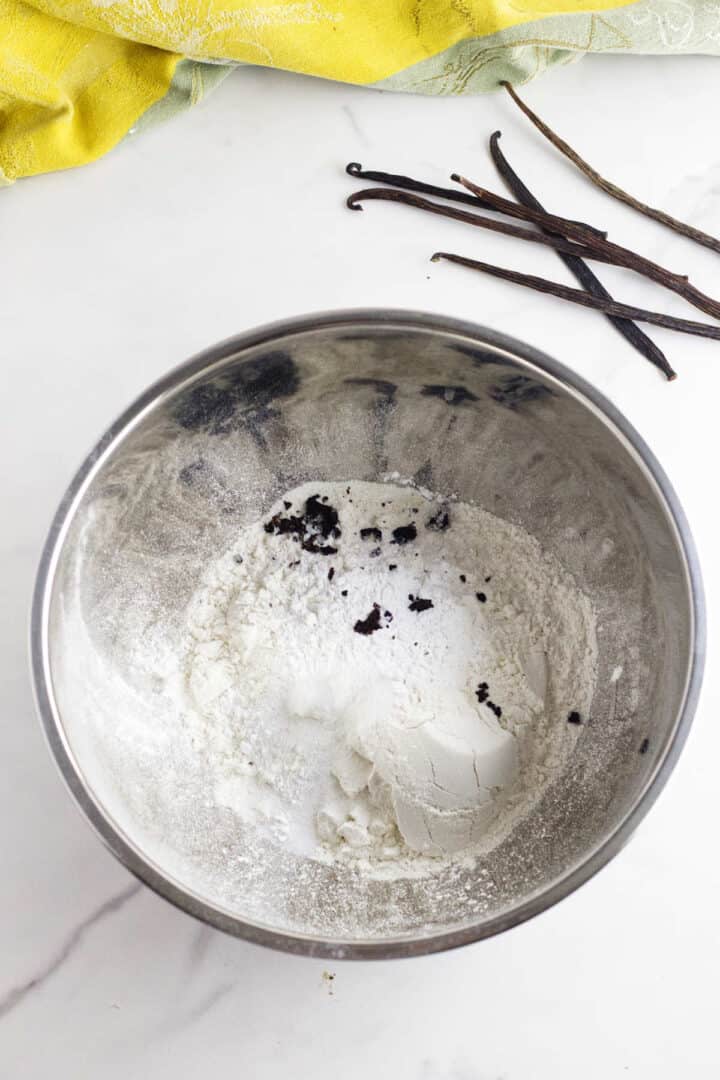 A bowl of white powder and vanilla sticks, perfect for crafting delicate vanilla bean scones.