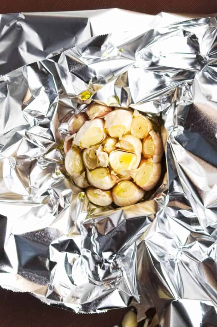 A head of garlic with the top sliced off, drizzled with oil, sits on crinkled aluminum foil-perfect for adding rich flavor to homemade roasted garlic focaccia.