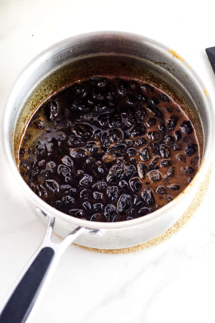 Raisins simmering in a dark molasses and spice mixture in a saucepan.