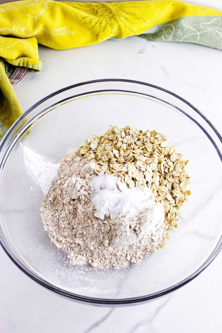 Whole wheat flour, all-purpose flour, oats, and leaveners in a glass mixing bowl.
