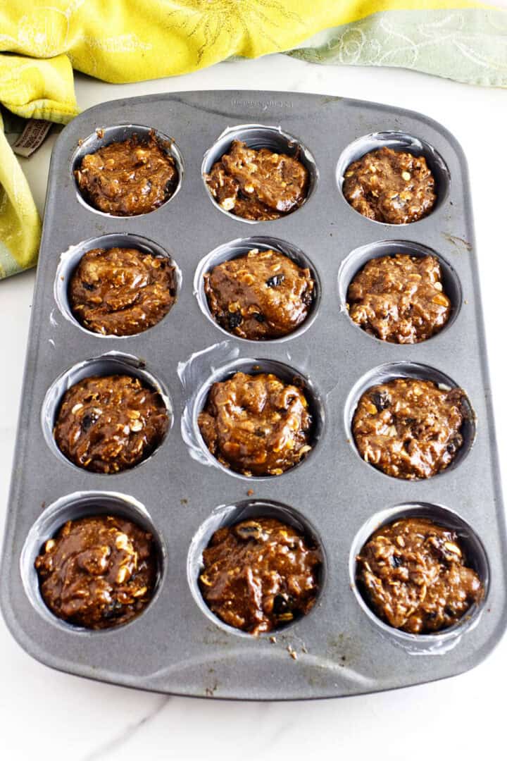 Twelve portions of unbaked Sailor Jack batter in a greased muffin pan.