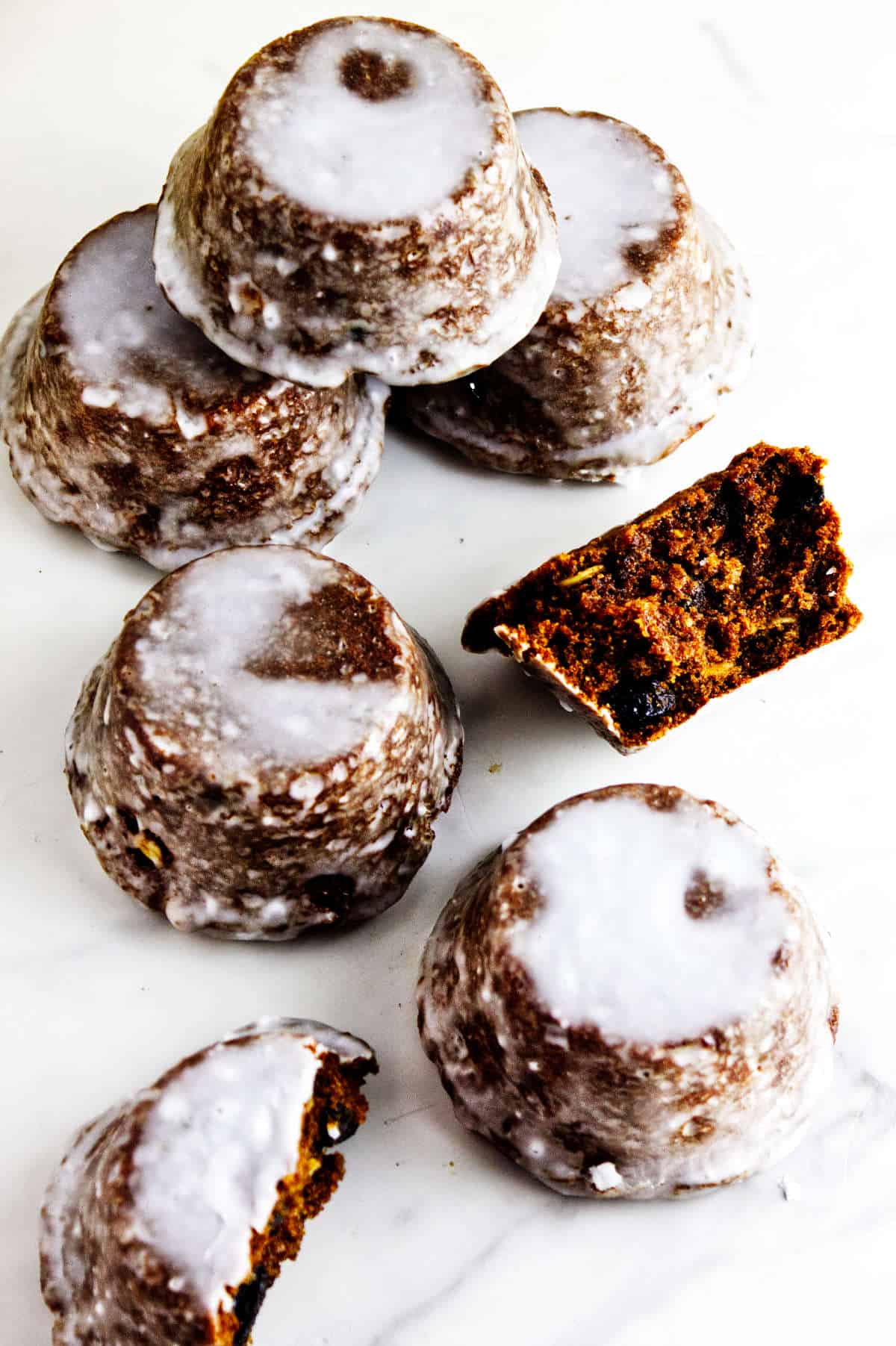 Glazed Sailor Jack muffins on a white surface, including cut cakes showing their dark raisin crumb.