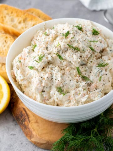A bowl of smoked salmon dip sits on a wooden board.
