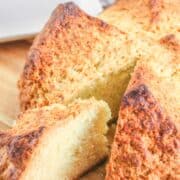 A close-up of freshly baked Irish soda bread on a wooden cutting board, made using a traditional Irish soda bread recipe. One slice is partially cut and pulled away, revealing the golden-brown crust and soft, crumbly interior.