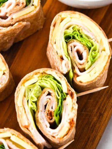Close-up of turkey and cheese pinwheels filled with deli meat, lettuce, and cheese, sliced and arranged on a wooden board with toothpicks holding them together.