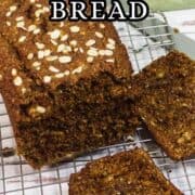 A loaf of Irish brown bread topped with oats sits on a cooling rack. Two slices are cut and laid in front of the loaf. Text reads “Irish Brown Bread.” Website "IKneadBread.com" is at the bottom.