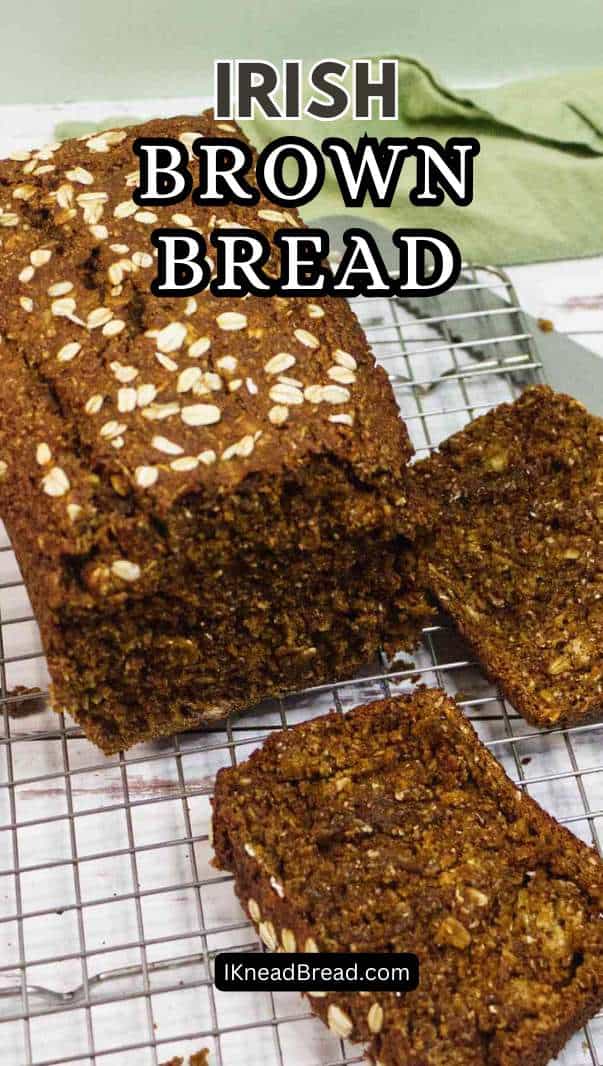 A loaf of Irish brown bread topped with oats sits on a cooling rack. Two slices are cut and laid in front of the loaf. Text reads
