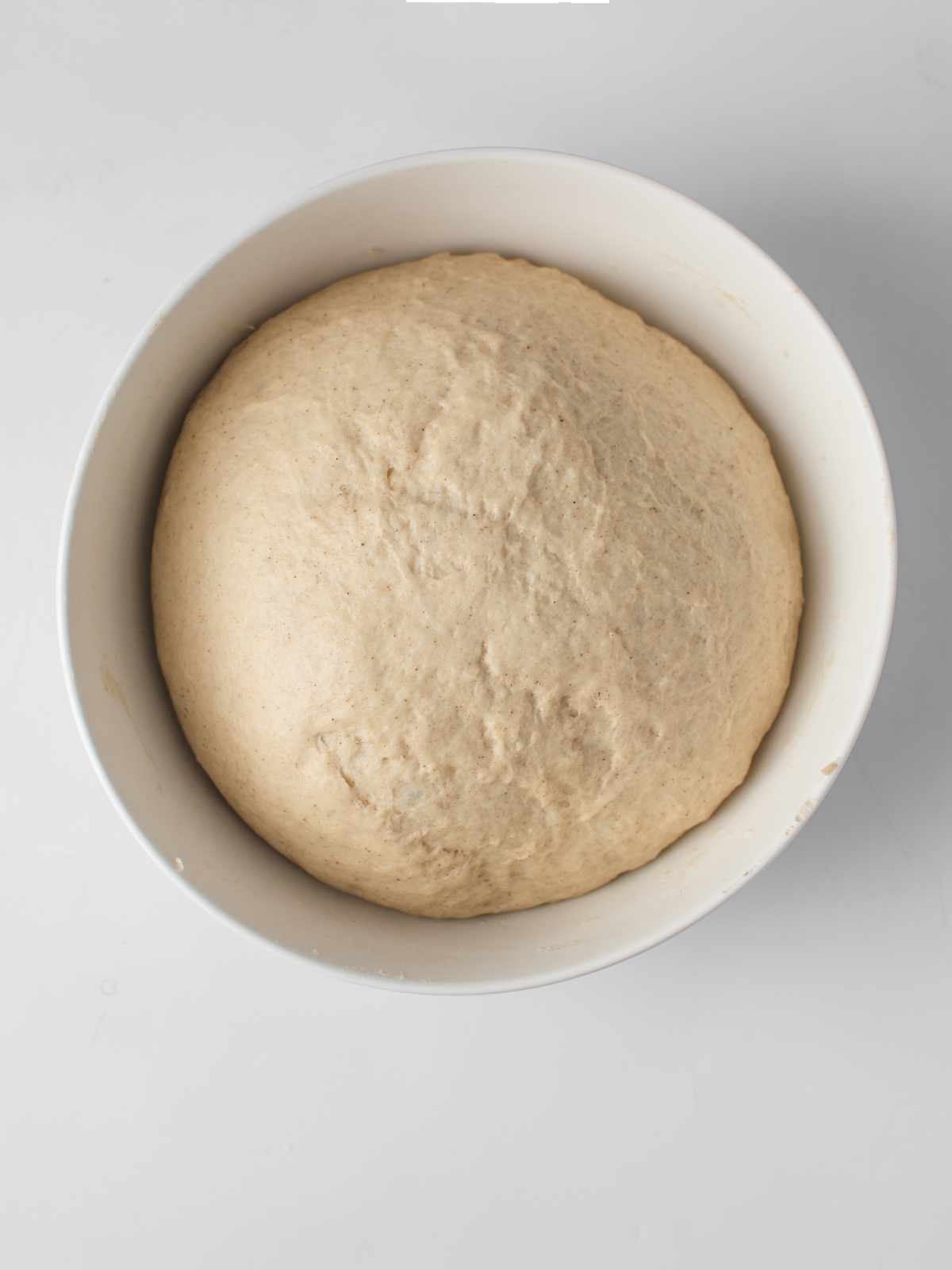 A white bowl filled with risen mantou buns dough, smooth and slightly domed, sits on a light grey surface.
