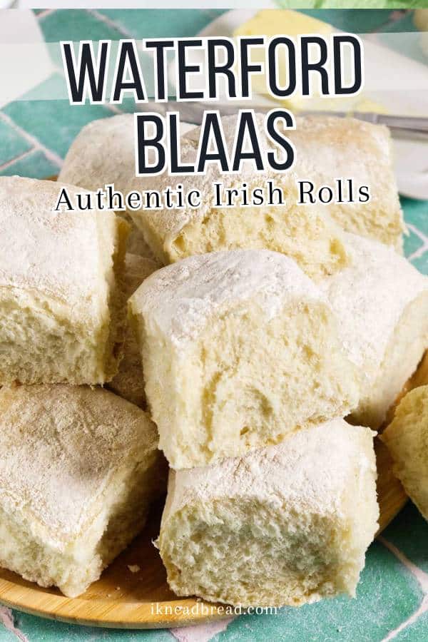 A close-up of a plate piled with fluffy, flour-dusted Waterford Blaas, traditional Irish bread rolls, with the text "Waterford Blaas Authentic Irish Rolls" overlaid on the image.