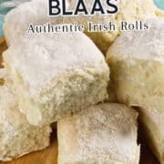 A wooden plate holds several flour-dusted, square Irish bread rolls called Waterford Blaas. Text overlay says, "WATERFORD BLAAS Authentic Irish Rolls" and "ikneadbread.com" at the bottom.